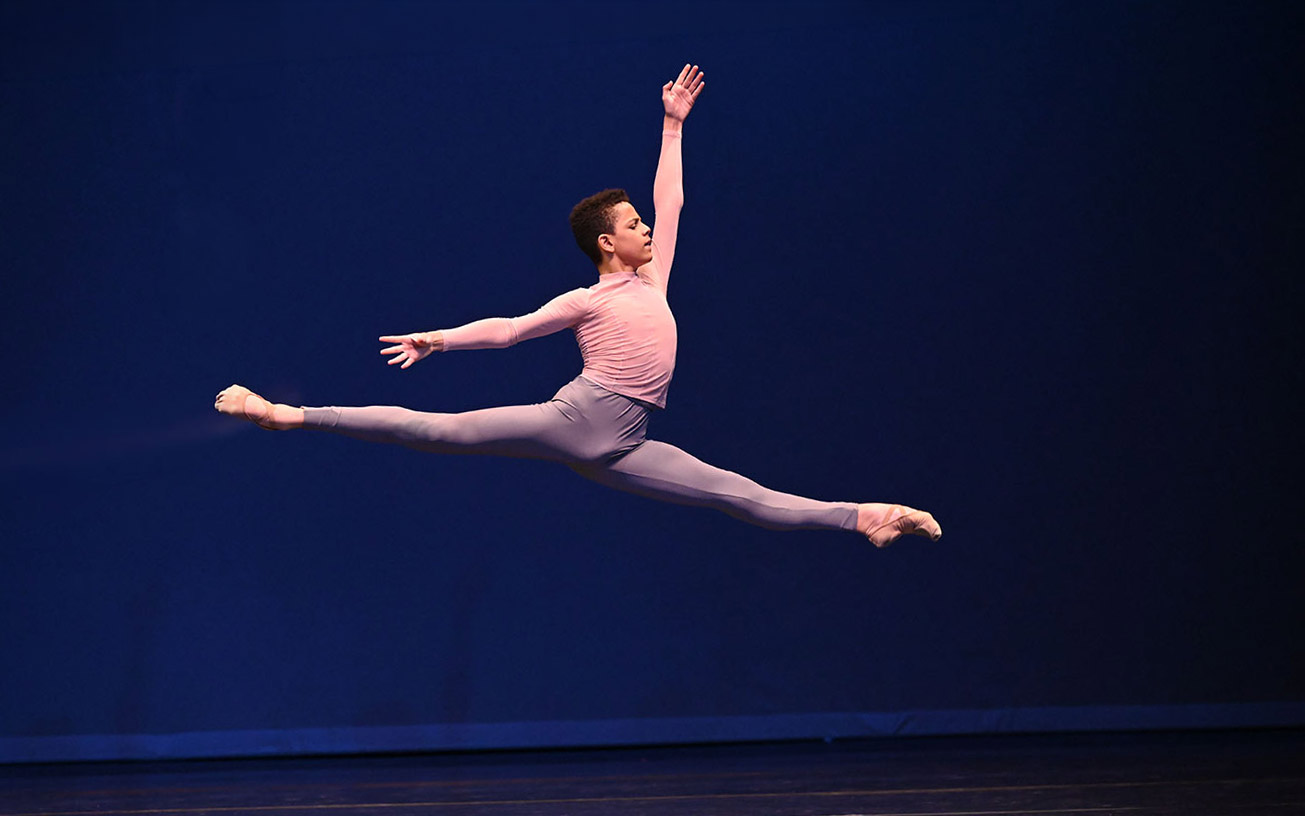 Male dancers split jumps in the air across stage